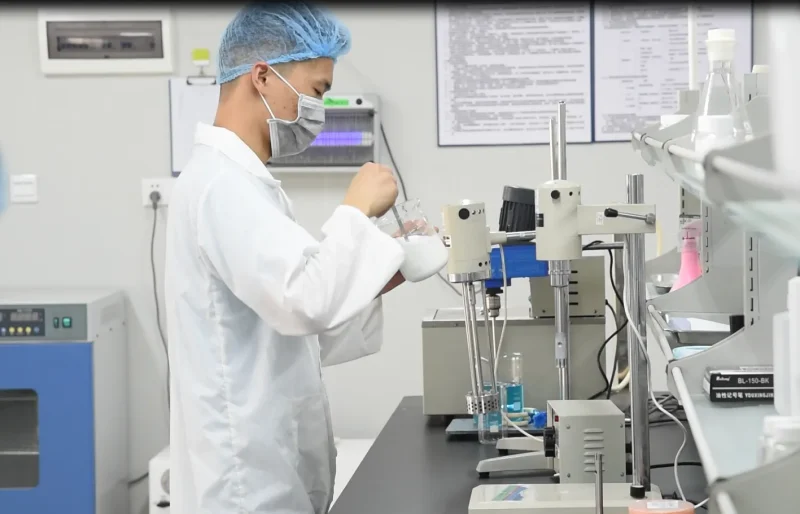A technician working in a clean haircare R&D laboratory, preparing formulations with beakers and mixers for private label hair care product development.