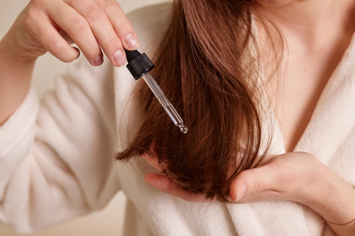 A person applying a nourishing aromatherapy hair care oil to hair ends using a dropper, featuring essential oils for hair growth and moisture.