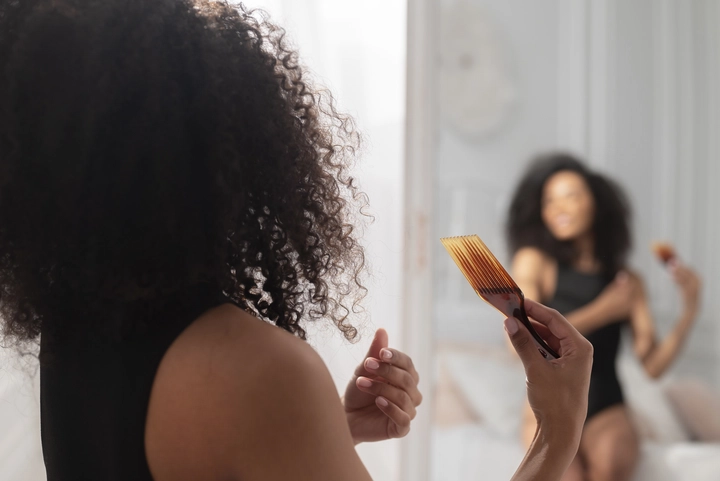 A Black woman is styling her curly hair in front of the mirror