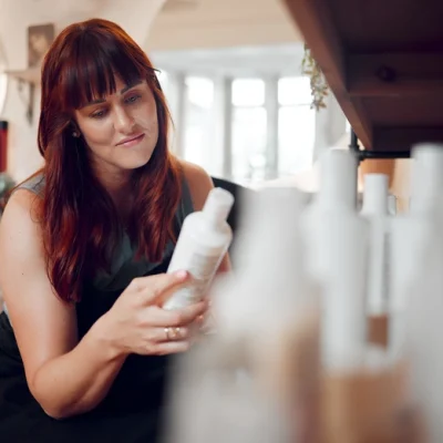 A woman examining a white bottle of private label hair care product among several options in a bright indoor setting.